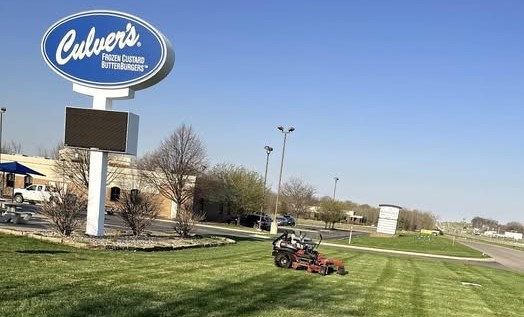 Zero-turn mower on a freshly striped commercial lawn in front of a Culver's sign