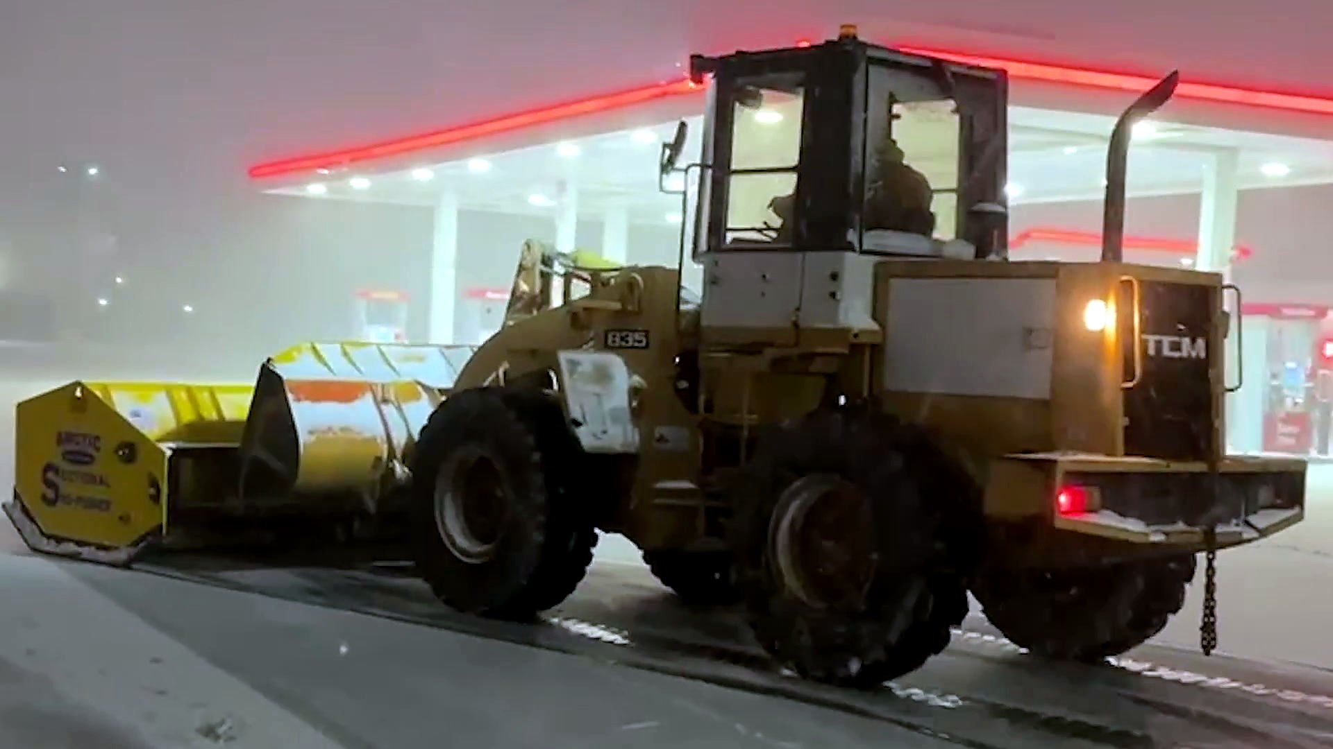 Wheel loader with an Arctic sectional sno-pusher clearing a commercial lot at night