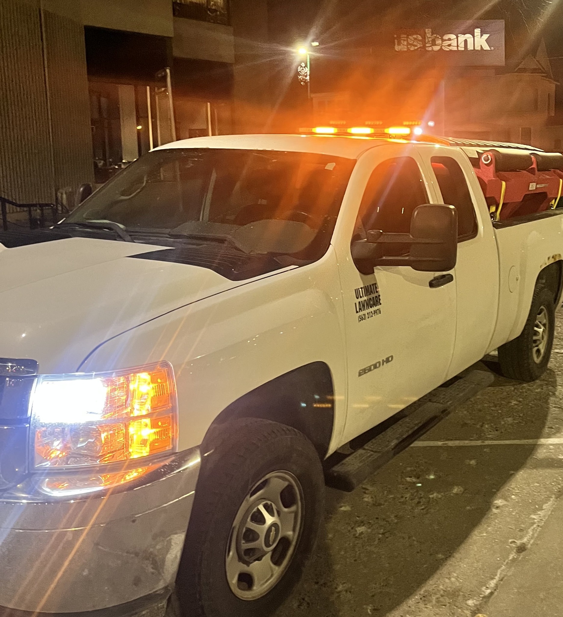 Ultimate Lawncare plow truck with salt spreader and beacon lights at night