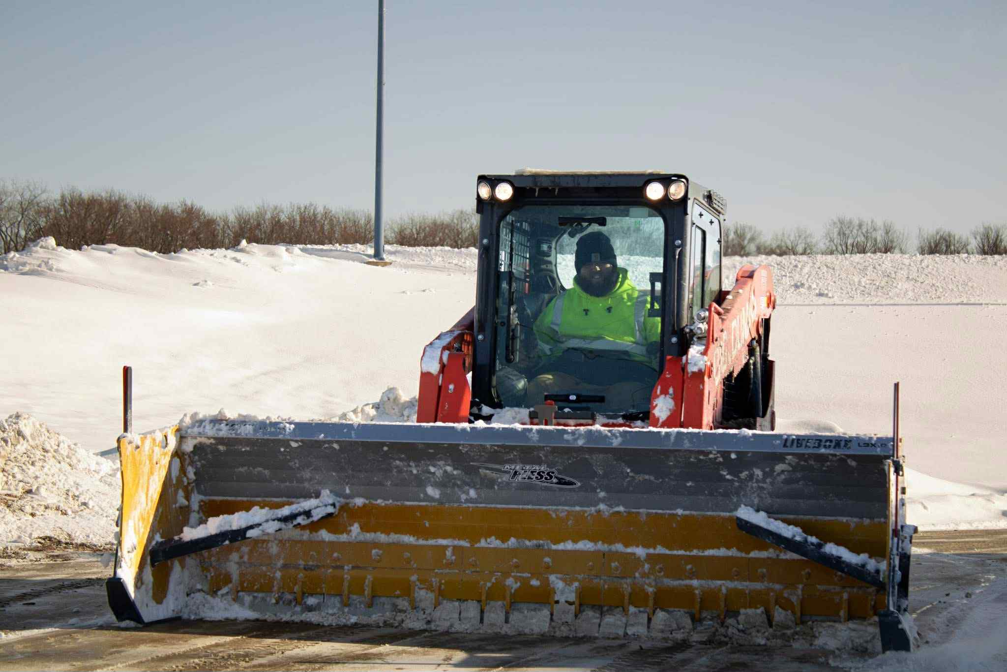 Track loader with a Metal Pless box plow clearing snow from a commercial lot